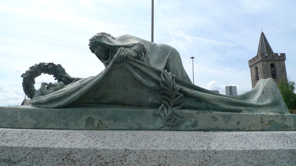 Groupe sculpté. Vue de face. La femme remonte le linceul qu'orne une palme.