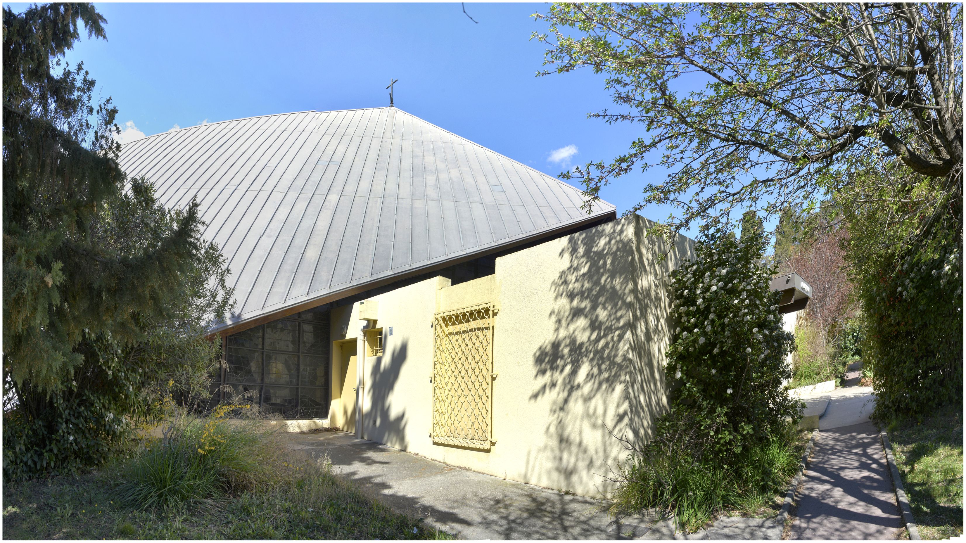Côté sud, bâtiment rectangulaire accolé à la structure, abritant l’entrée, une salle de catéchisme et une chapelle de semaine.
