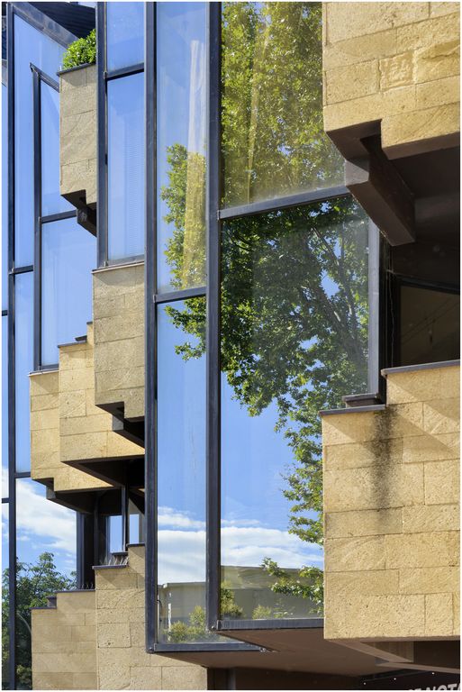 Façade sur l’avenue. Vue latérale. Jeu sur le contraste pierre calcaire et verre réfléchissant la verdure.