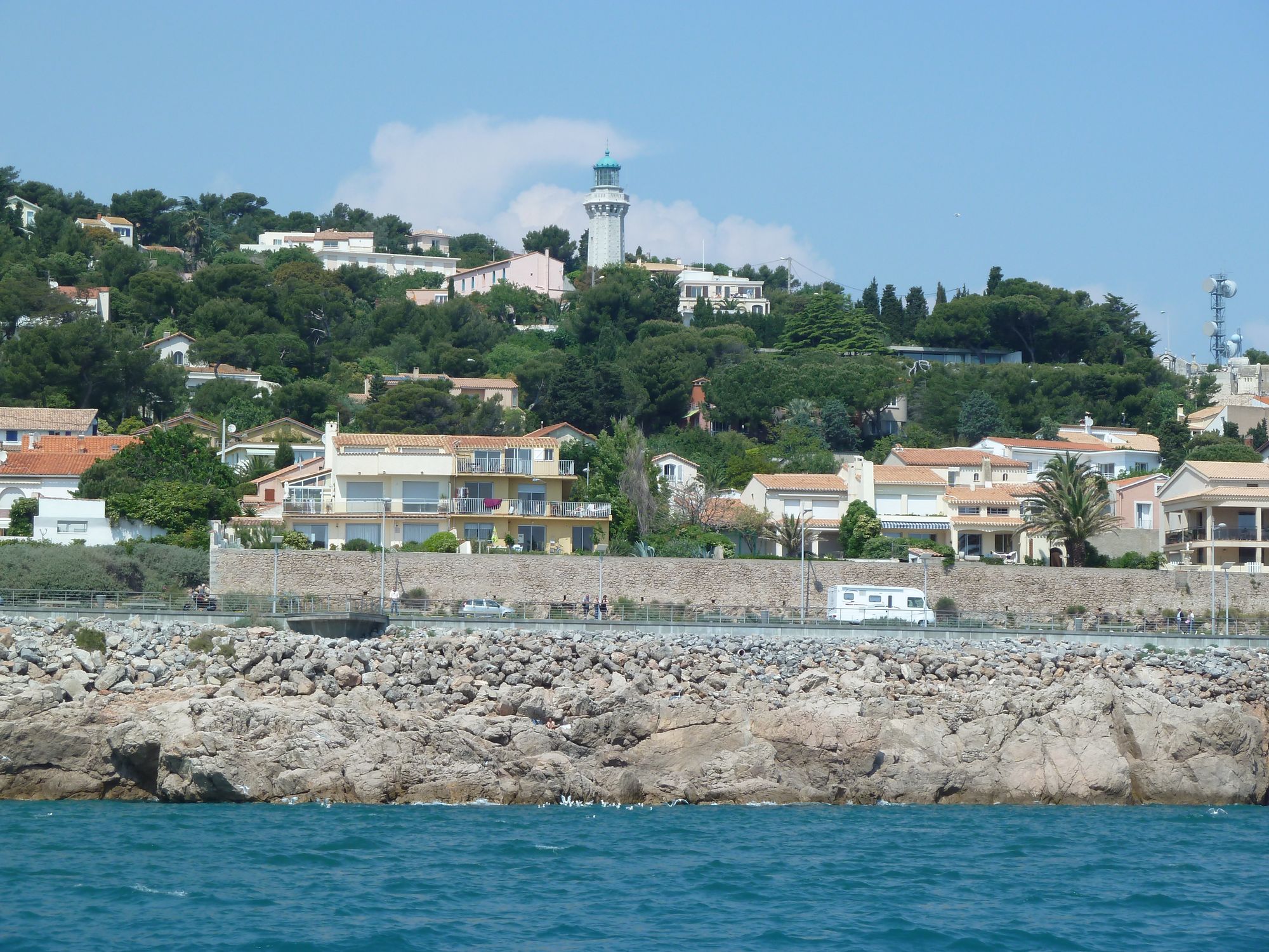 Vue de la villa depuis la mer, cachée par la végétation, un peu en dessous du phare Saint-Clair. On aperçoit uniquement le bandeau horizontal de son toit terrasse.