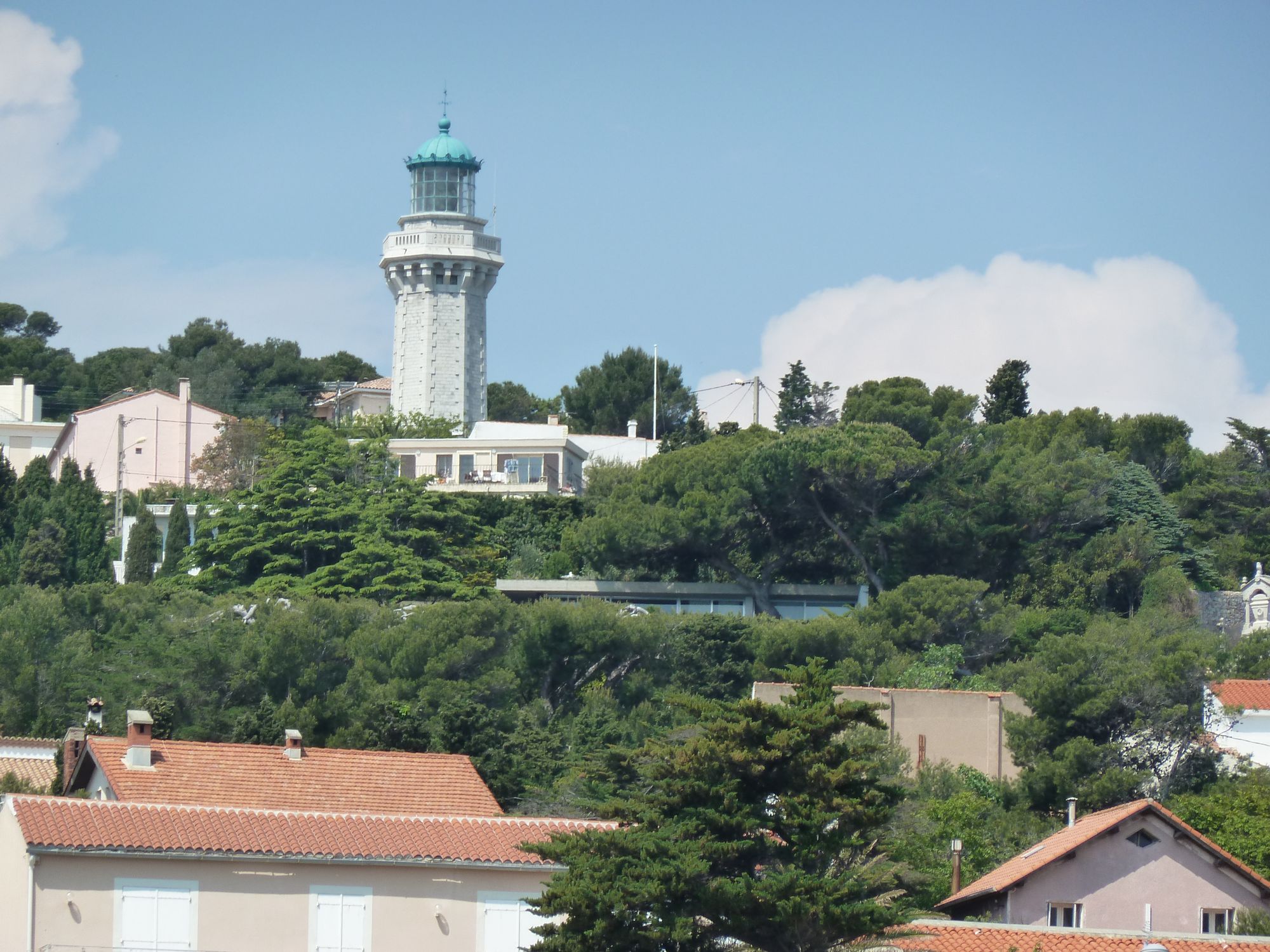 Vue de la villa depuis la mer, cachée par la végétation, un peu en dessous du phare Saint-Clair. On aperçoit uniquement le bandeau horizontal de son toit terrasse.