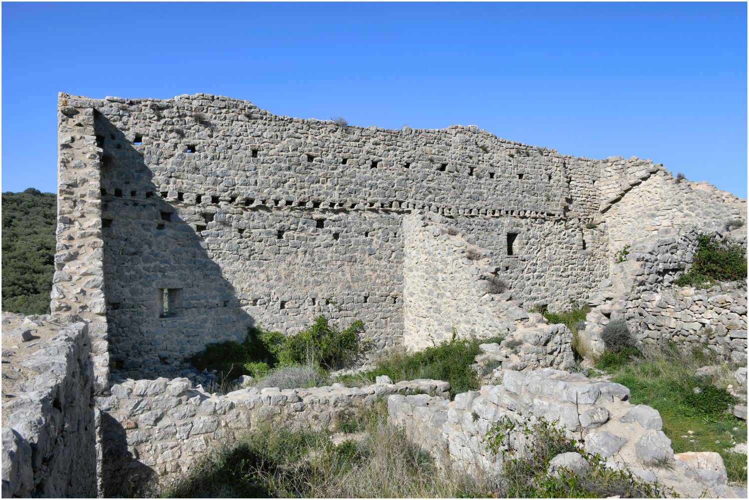 Vue intérieure de l’enceinte côté Nord, percée d’une archère et de trous de boulins correspondant à des maisons adossées.