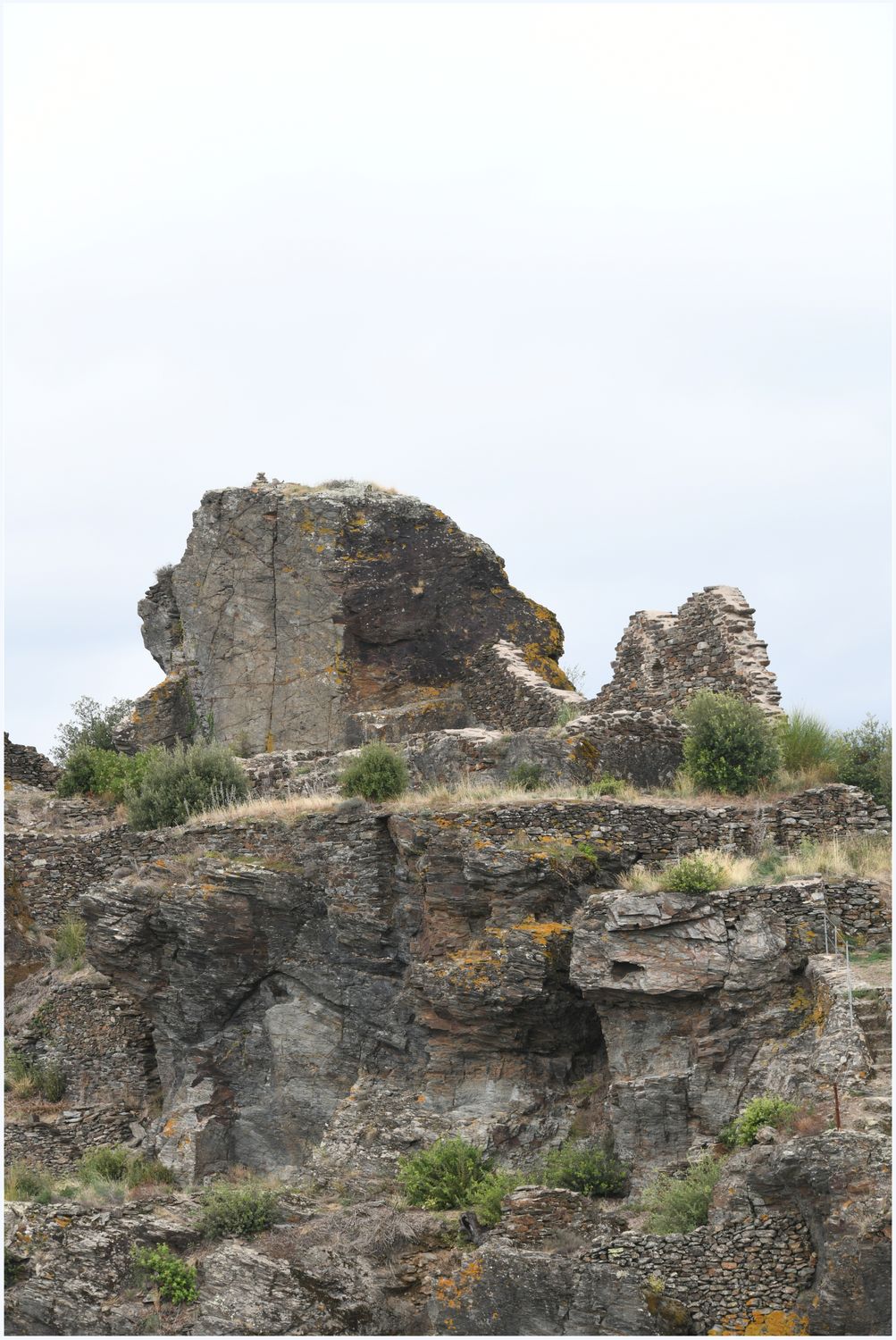 Vue d’ensemble du pôle castral primitif, avec au sommet le socle rocheux retaillé et en contrebas des habitations adossées au rocher.