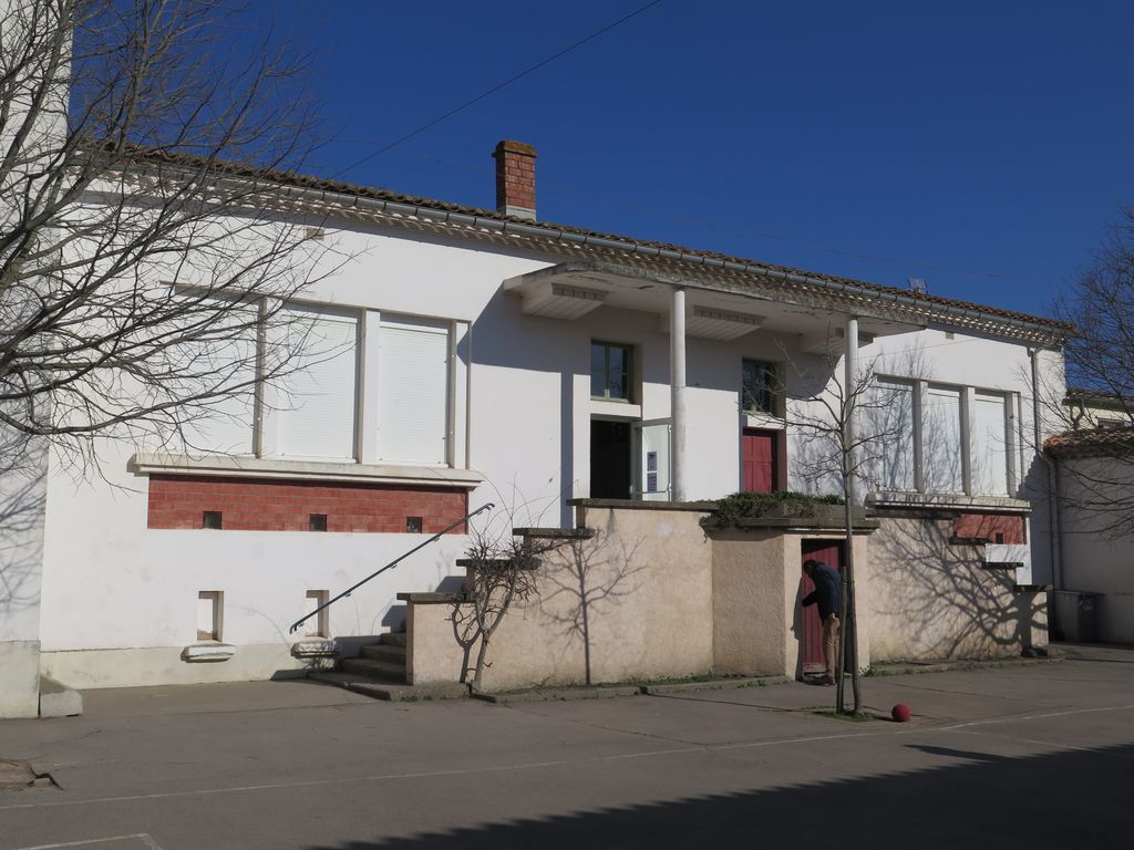 Façade sur la cour de récréation. Sortie des élèves dans la cour protégée par un auvent.