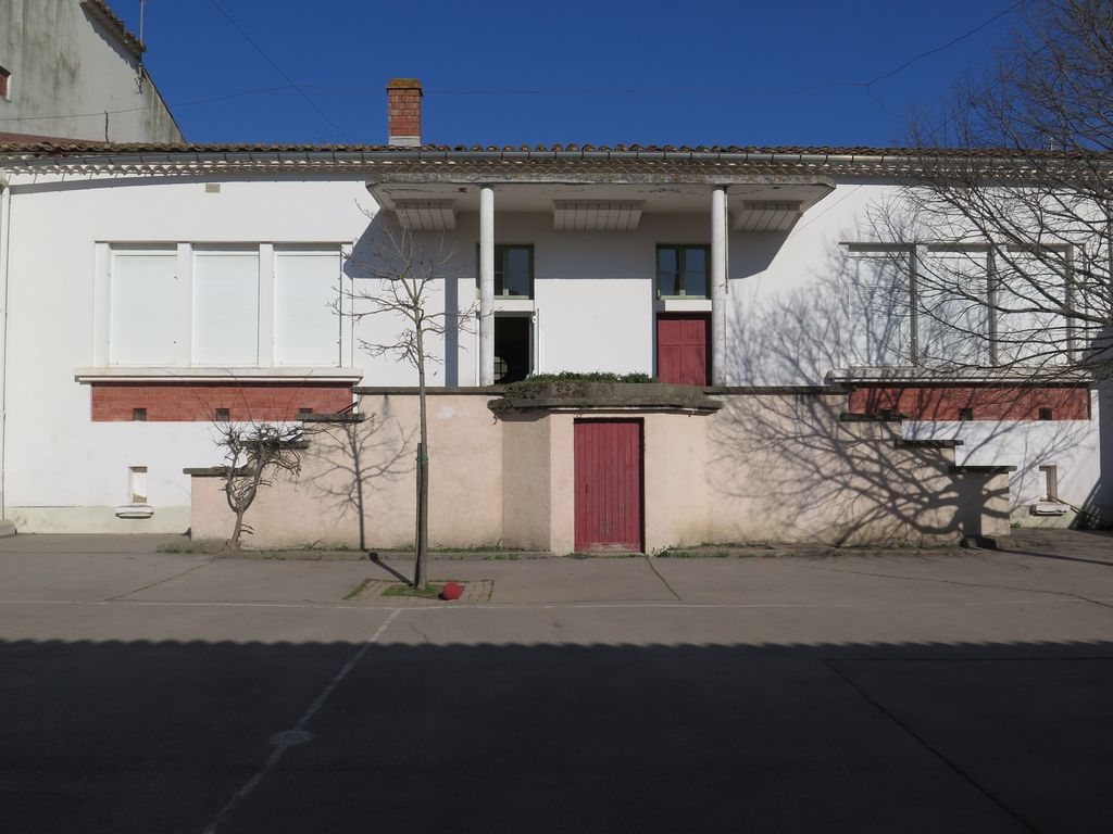 Façade sur la cour de récréation. Sortie des élèves dans la cour protégée par un auvent.