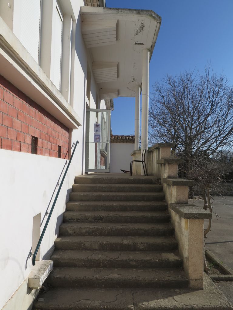 Façade sur la cour de récréation. Escalier d’accès et auvent de la porte.