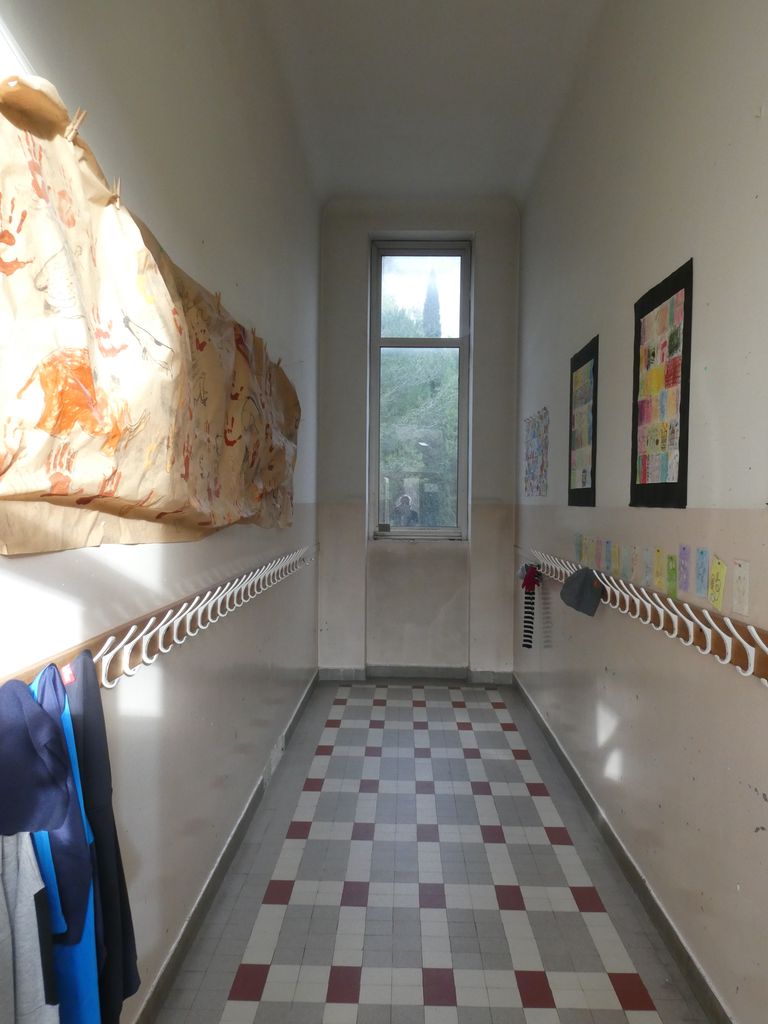 Couloir des classes, éclairé à l’extrémité par une fenêtre étroite.