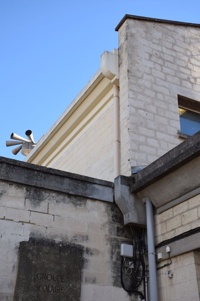 Ecole élémentaire Jean-Moulin. Façade sur rue. Détail des parements pierre et moulures et corniche en béton lisse.