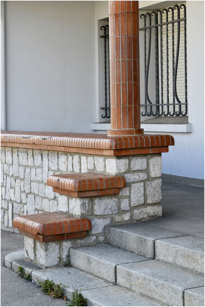 Façade sur rue. Entrée de l’école maternelle. Moellons de pierre et briques aux angles arrondis.