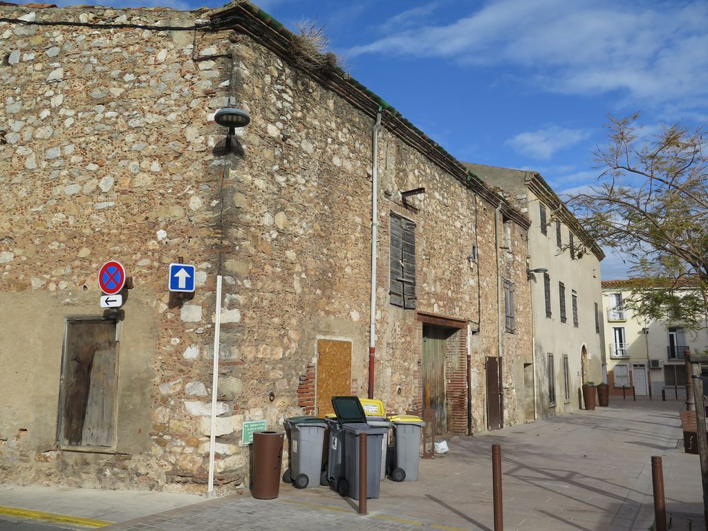 Façade sur la place : au premier plan, les dépendances, au second plan la maison avec son enduit blanc.