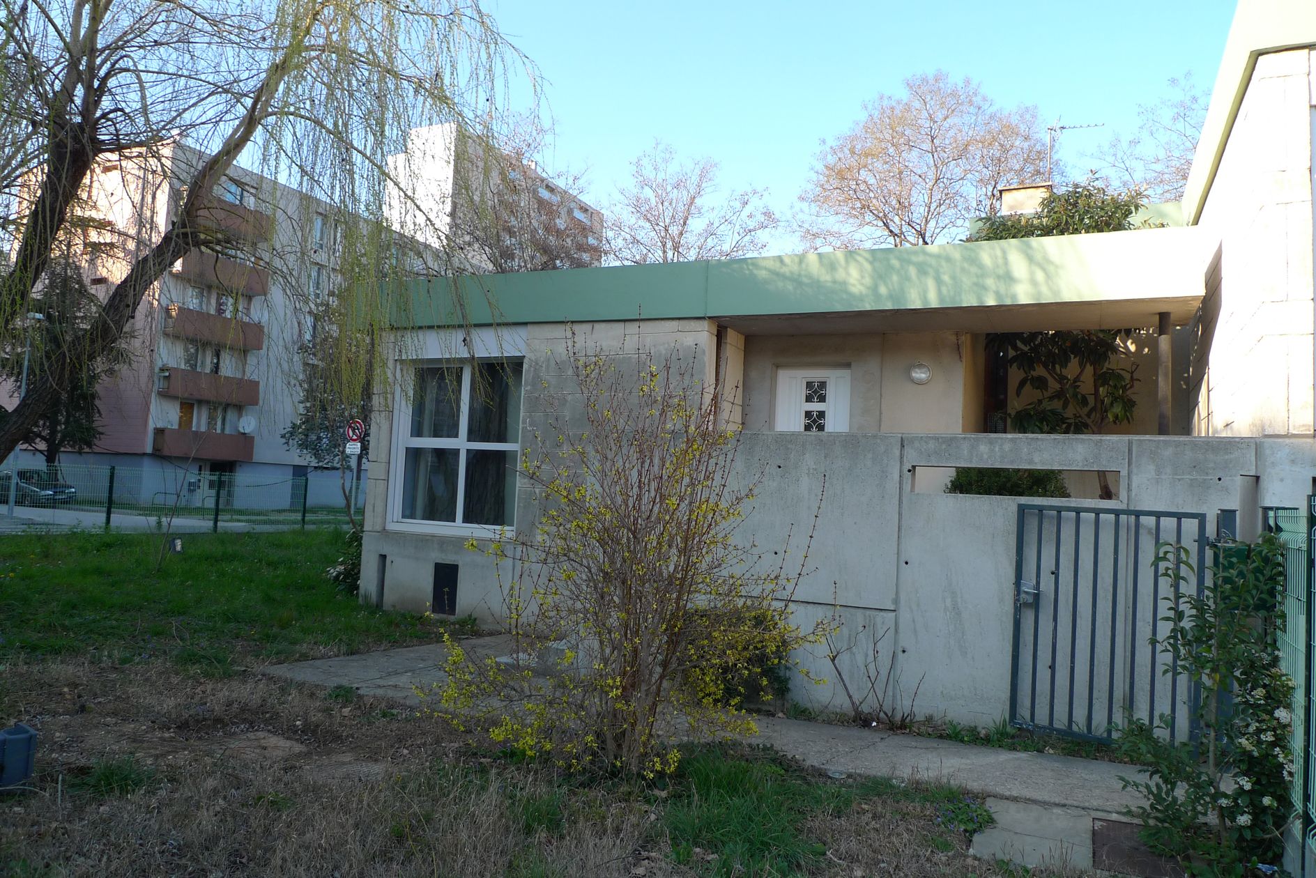 Entrée et jardin sur la placette ; en arrière-plan le quartier des Escanaux sur l’avenue de la Mayre.