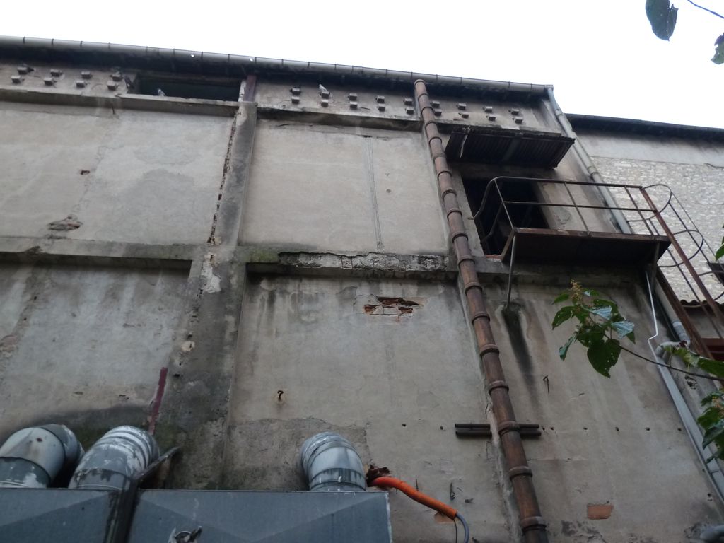 Façade arrière. En cœur d’ilot, résille poteaux poutre en béton armé et remplissage en brique creuse + enduit ciment motifs sous le toit