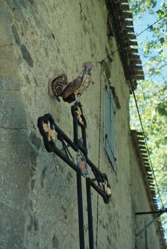 Croix en fer forgé à côté de la porte fortifiée des anciens remparts du Nord-Ouest. Détail du coq.