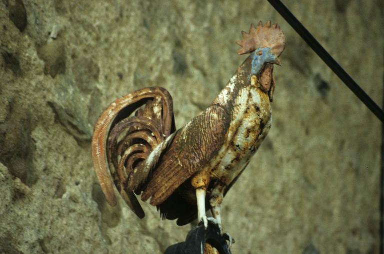 Croix en fer forgé à côté de la porte fortifiée des anciens remparts du Nord-Ouest. Détail de la partie haute. Le coq en fer forgé peint.