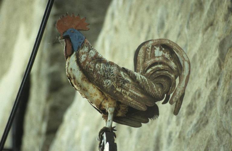 Croix en fer forgé à côté de la porte fortifiée des anciens remparts du Nord-Ouest. Détail de la partie haute. Le coq en fer forgé peint.