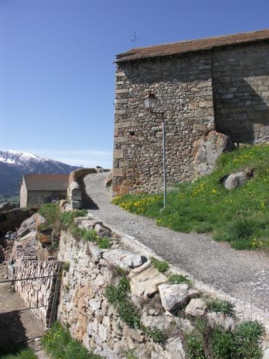 Accès à l'église par le côté est : muraille du castrum au 1er plan.