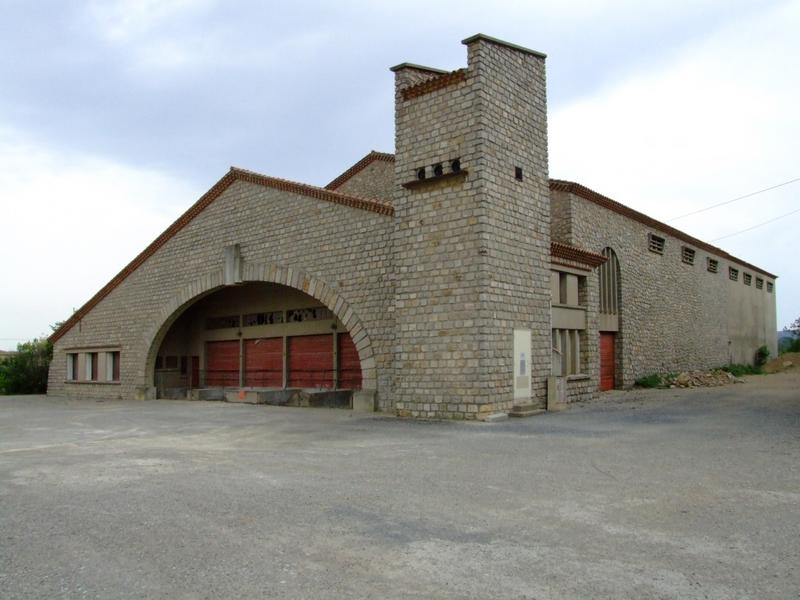 Vue de trois-quarts droits de la cave coopérative. Les bureaux se distinguent derrière le faux pigeonnier qui abrite le transformateur.