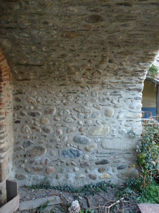 Cour intérieure. Accès depuis le couloir, par un grand arc surbaissé, portant la galerie de l'aile sud. Murs latéraux en galets.