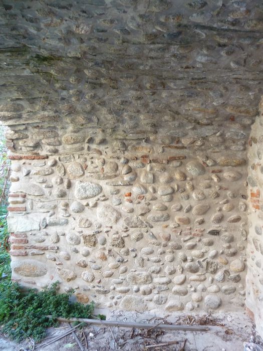 Cour intérieure. Accès depuis le couloir, par un grand arc surbaissé, portant la galerie de l'aile sud. Murs latéraux en galets.