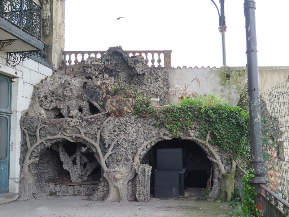 Rocaille en faux bois de ciment armé. Armes et inscription : travail et progrès, avec une fontaine au centre.