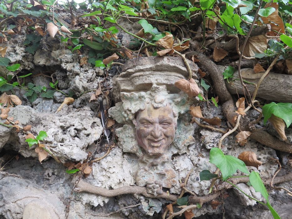 Têtes en terre cuite sur le thème de la vigne décorant la rocaille en faux bois.