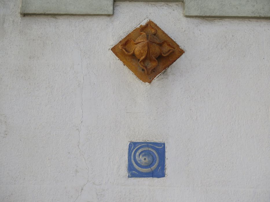 Carreaux de grès émaillé, Art Nouveau. Chaque baie est marquée par deux cabochons en céramique, bleu et ocre, ponctuant les travées des cabines sous les appuis de fenêtres.