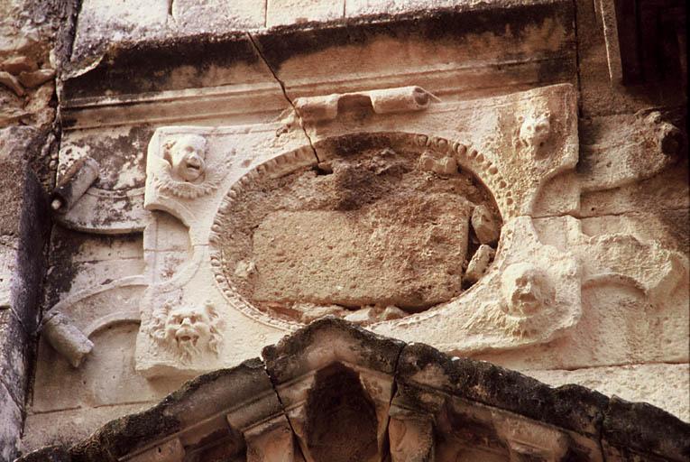 Vue de la façade ruinée sur la rue, cartouche au-dessus du portail.