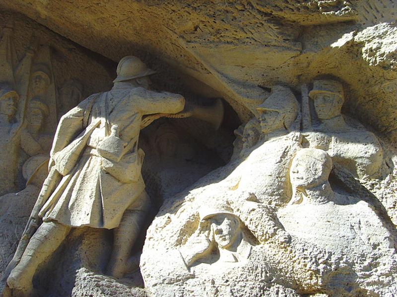 Vue du clairon de profil, sur sa droite se tient un groupe de 4 soldats taillés en bas-reliefs ; ils représentent " les manes des héros qui dorment dans le caveau et qui s'éveillent à chaque appel du Souvenir pour répondre : présent ".