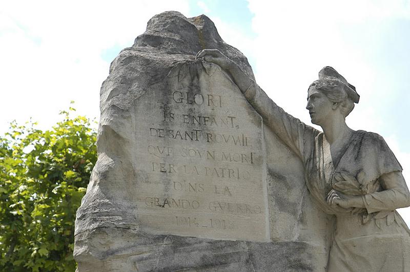 Détail de la face antérieure ; la provençale personnifiant la Ville, tient d'un côté une gerbe de laurier et dépose un rameau d'olivier au-dessus de la dédicace en langue provençal inscrite en caractères romains signifiant " Gloire aux enfants de Saint Rémy qui sont morts pour la patrie dans la grande guerre 1914-1918 ".