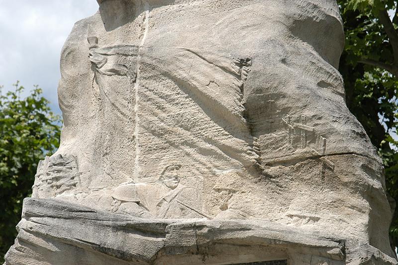 Détail de la face postérieure ; le bas-relief réalisé au dessus de la veuve représente un assaut de poilus. Un drapeau déployé au centre de la scène, des croix dans un cimetière à droite, une barricade en bois de l'autre côté évoque une tranchée.