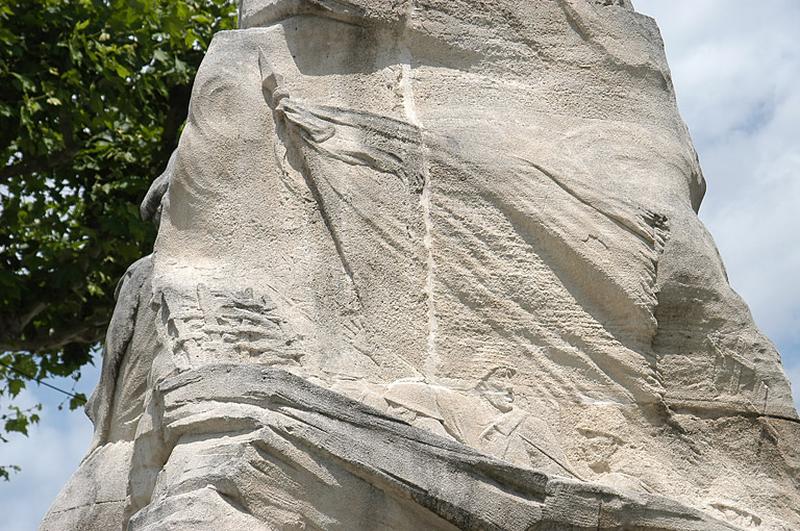 Vue du bas-relief, le ciel est nuageux au-dessus du drapeau, les barricades sont représentées par un treillage de bois.