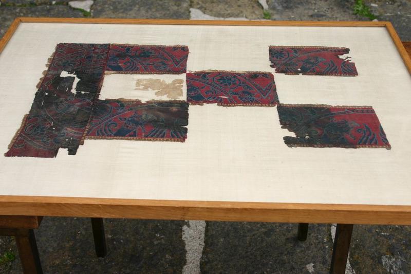 pièce de tissu de style byzantin, assemblage de six fragments rectangulaires à fond rouge, ornés de motifs bleu marine ourlé de bleu clair : végétaux ( fleurs et feuillages  en arabesques associés à des oiseaux et des griffons, vue générale ) - © Ministère de la Culture (France), Conservation des antiquités et objets d'art de Haute-Loire, tous droits réservés