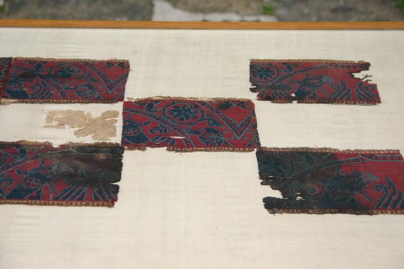 pièce de tissu de style byzantin, assemblage de six fragments rectangulaires à fond rouge, ornés de motifs bleu marine ourlé de bleu clair : végétaux ( fleurs et feuillages  en arabesques associés à des oiseaux et des griffons, vue partielle ) - © Ministère de la Culture (France), Conservation des antiquités et objets d'art de Haute-Loire, tous droits réservés