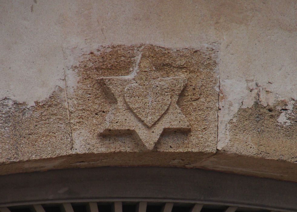 Église. Transept sud (élévation ouest) : cœur inscrit dans une étoile à 6 branches sculpté sur l’arc segmentaire de la porte.